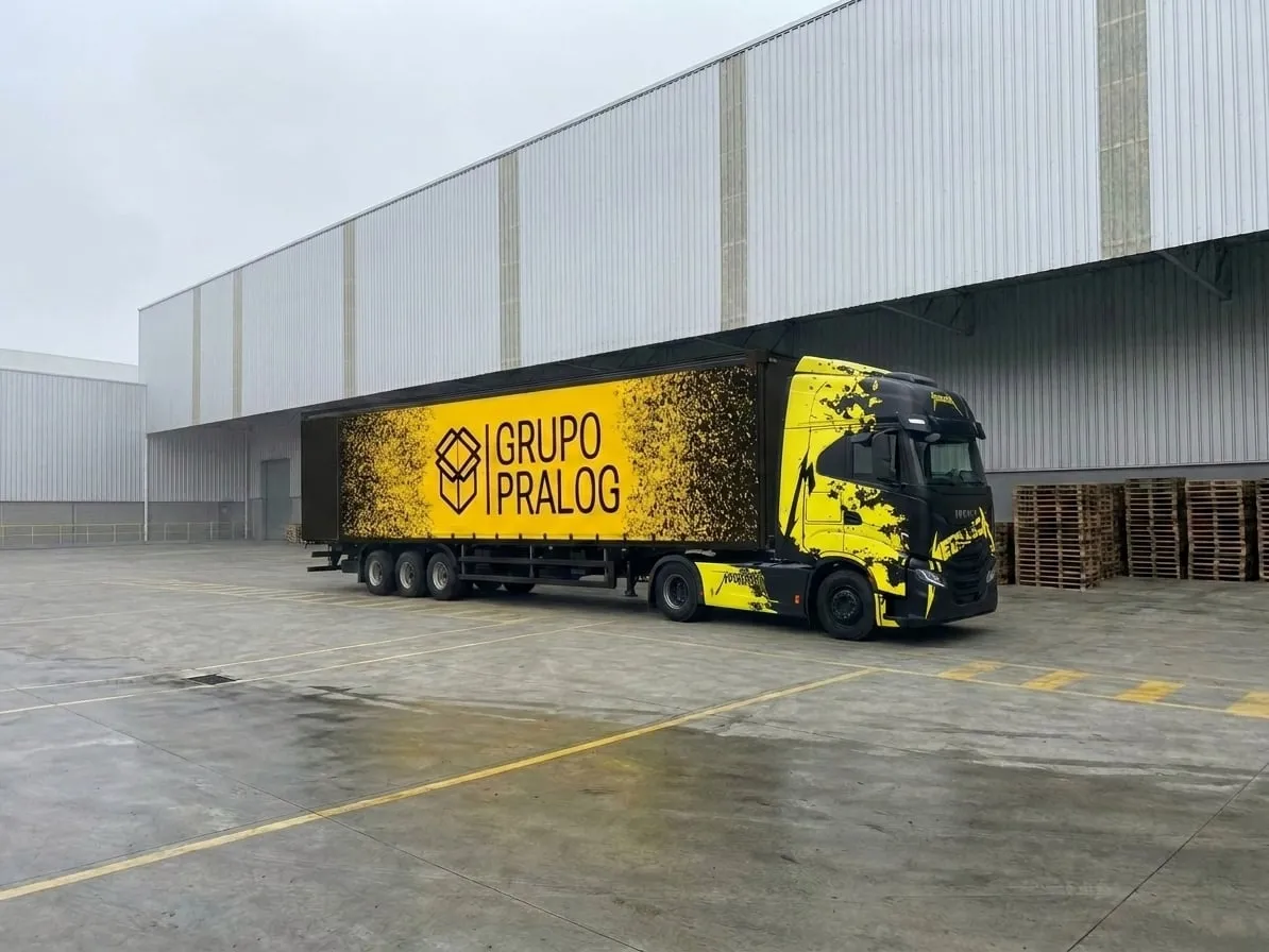 Carreta sider Iveco S-Way da frota PRA LOG em pátio industrial com pallets ao fundo